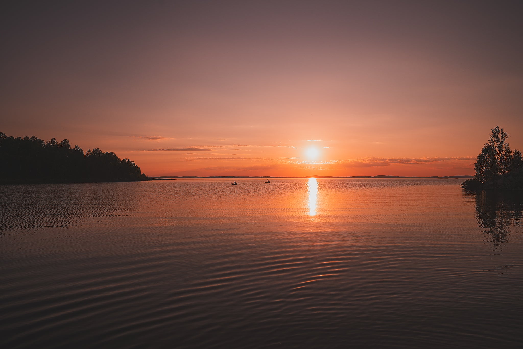 Coucher de soleil orangé sur un lac calme du Québec, deux kayaks silhouettés au loin sur l'eau